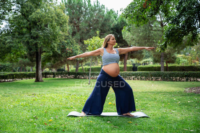Улыбающаяся беременная привлекательная женщина тренируется на коврике в парке — стоковое фото