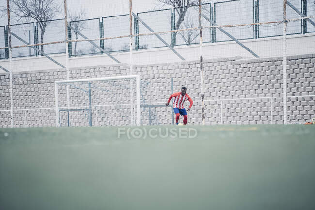 African soccer player with red and white equipment playing soccer. — Stock Photo