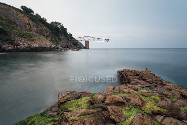 Amazing view of modern unfinished bridge located near cliff over calm water — Stock Photo