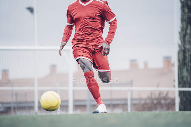Jugador de fútbol africano con traje rojo jugando fútbol. - foto de stock