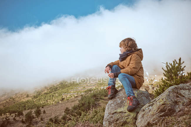 Ragazzo seduto vicino alla collina il giorno nebbioso — Foto stock