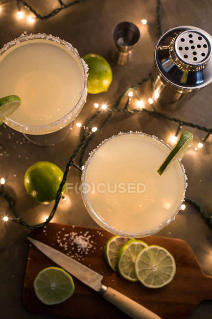 Copas de cóctel de margarita sobre mesa iluminada con ingredientes - foto de stock