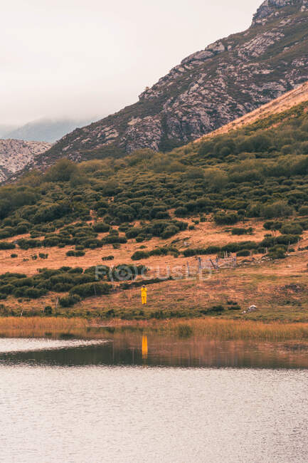 Pessoa de capa de chuva amarela que vai à margem do lago perto de uma montanha em Isoba, Castela e Leão, Espanha — Fotografia de Stock