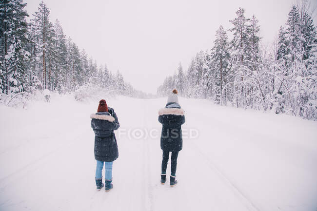 Rückansicht von zwei Damen in warmer Kleidung, die auf verschneiten Straßen stehen und spektakuläre arktische Landschaften fotografieren — Stockfoto