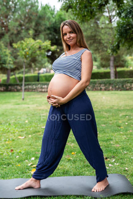 Lächelnd schwangere attraktive Frau trainiert auf Matte im Park — Stockfoto