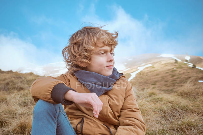 Cute boy sitting on hill near brook — Stock Photo