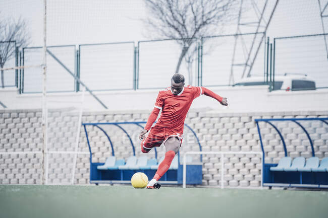 Joueur de football africain avec tenue rouge jouant au football. — Photo de stock