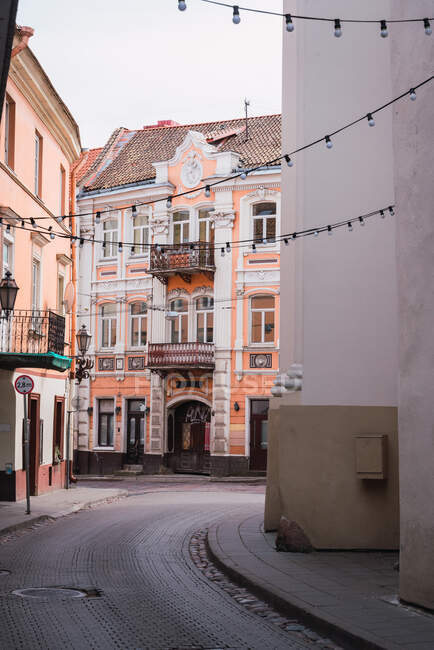 Гірлянди з лампочками, що звисають між красивими будівлями на вузькій вулиці старого міста — стокове фото
