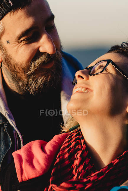 Homem barbudo abraçando mulher alegre perto de madeira na floresta no fundo borrado — Fotografia de Stock