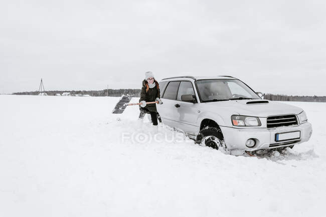 Женщина с лопатой возле машины на снежном поле — стоковое фото