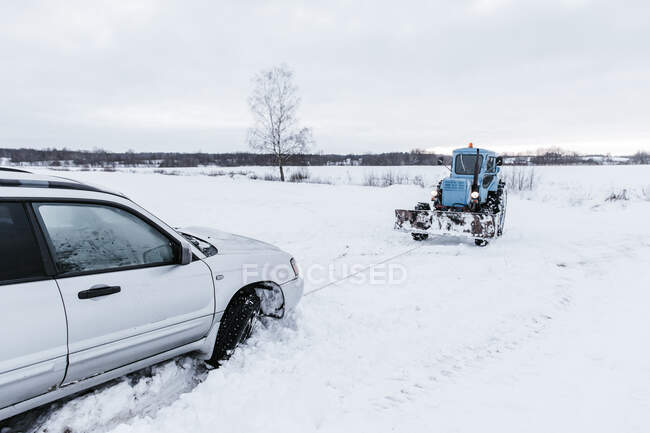 Tractor remolcando el automóvil roto de la nieve en el prado en Vilnius, Lituania - foto de stock