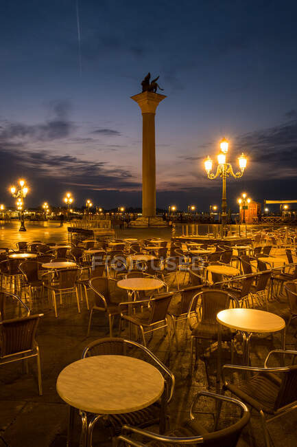 Runde Tische und bequeme Stühle stehen neben schönen Säulen auf dem beleuchteten Platz in bewölkten Abend in Venedig — Stockfoto