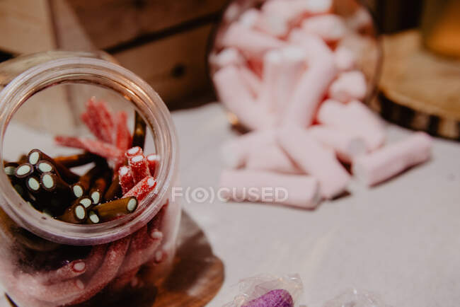 Deliciosos tubos de geléia em lata perto de marshmallows espalhados na mesa sobre fundo borrado — Fotografia de Stock