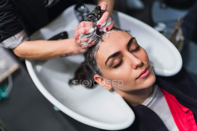 D'en haut femme laver les cheveux à dame attrayante avec les yeux fermés dans l'évier — Photo de stock