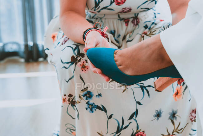 Кукурудзяна жінка в одязі, що допомагає носити взуття на нозі леді на розмитому тлі — стокове фото