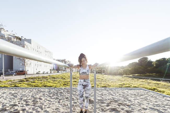 Приваблива жінка в спортивному одязі робить вправи на паралельних брусах на дворі біля будівель — стокове фото