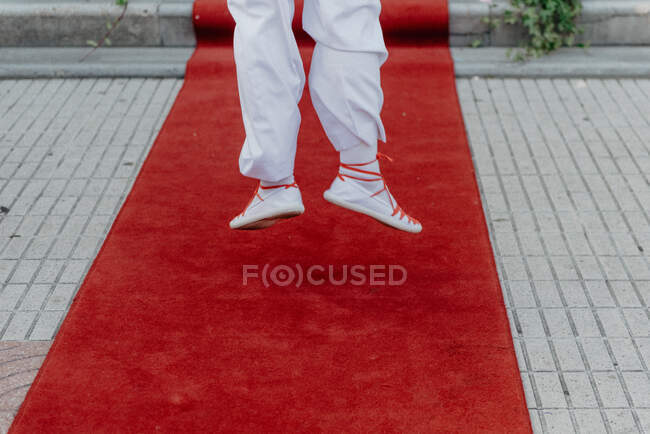 Вид ззаду на ноги людини в білому костюмі, що стрибає на червоному килимі на вулиці — стокове фото