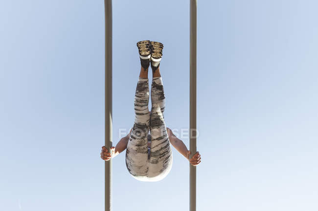 From below woman in sportswear doing exercises on parallel bars and blue sky — Stock Photo