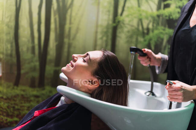 Жінка миє волосся до привабливої жінки з закритими очима в раковині. — стокове фото