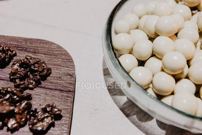 Dall'alto serie di caramelle bianche e dessert neri su piatto e asse su sfondo bianco — Foto stock