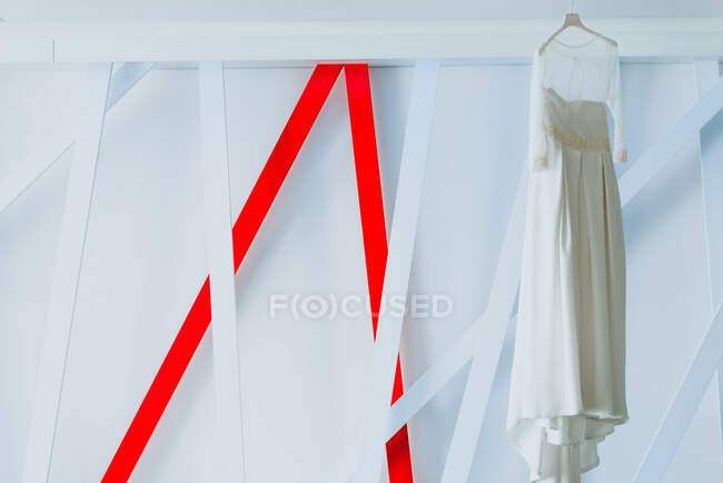 Концепция красивого светлого платья висит на вешалке рядом с абстрактными украшениями возле белой стены — стоковое фото