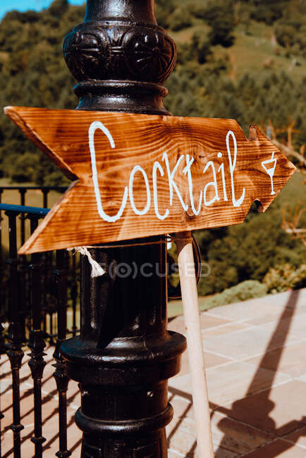 Wooden tablet with cocktail inscription placed on street near fence in sunny weather — Stock Photo