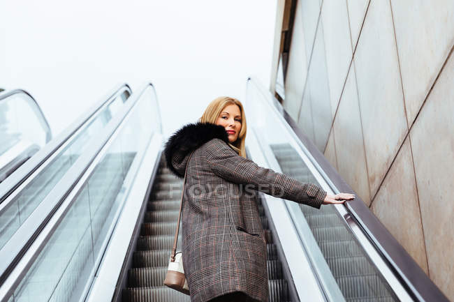 Chica rubia escalando escaleras mecánicas en el centro comercial - foto de stock