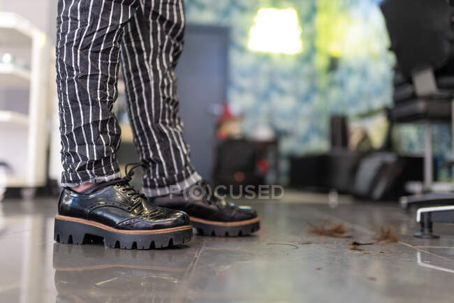 Vista lateral de las piernas de los cultivos en botas de estilista en peluquería sobre fondo borroso - foto de stock