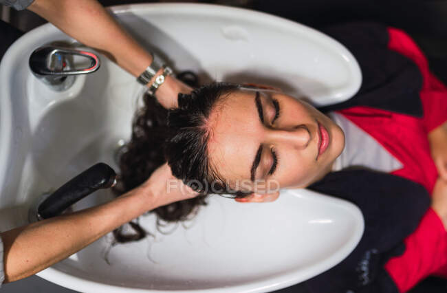 Da suddetto donna che lava capelli a signora attraente con occhi chiusi in lavandino — Foto stock