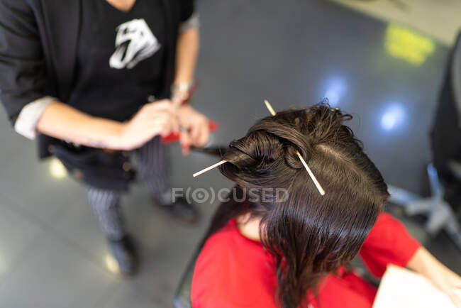 Estilista envejecida haciendo peinado a la joven atractiva en el salón de peluquería - foto de stock