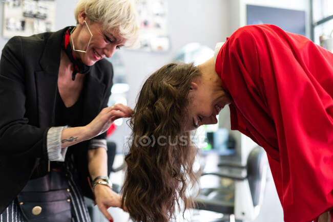 Старый стилист делает прическу привлекательной молодой леди в парикмахерской — стоковое фото