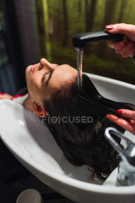 Зверху жінка миє волосся до привабливої леді з закритими очима в раковині — стокове фото