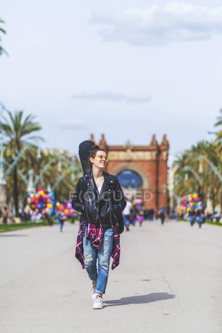 Vue de face d'une jeune hipster rieuse marchant dans un parc par temps ensoleillé en regardant ailleurs — Photo de stock