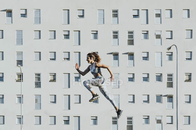 Side view of athletic woman levitating near building in sunny weather — Stock Photo