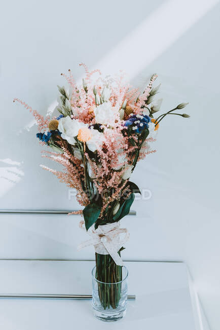 Ramo de hermosas flores aromáticas frescas en jarrón de vidrio cerca de la pared blanca - foto de stock