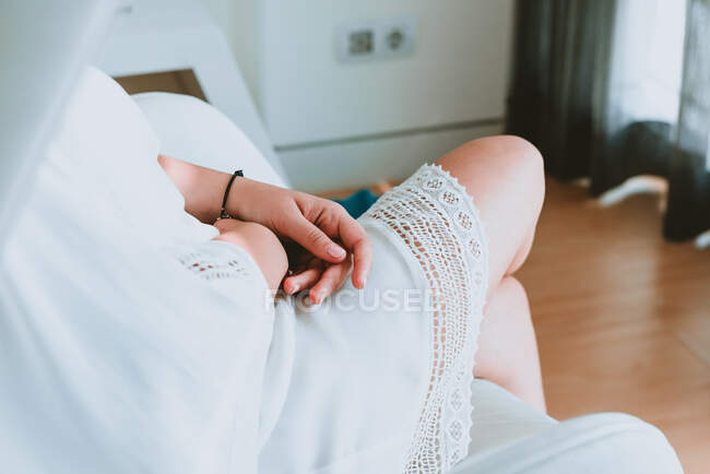 Vista lateral da colheita jovem senhora em vestido branco sentado no quarto no fundo borrado — Fotografia de Stock