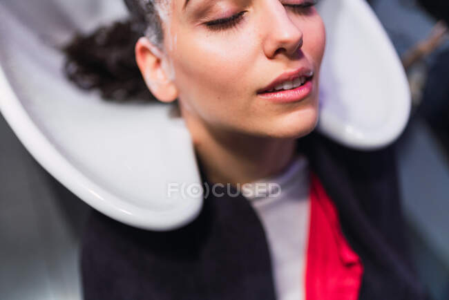 Зверху жінка миє волосся до привабливої леді з закритими очима в раковині — стокове фото