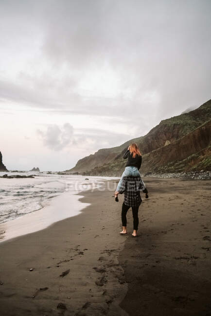 Unbekannter Mann trägt Frau auf Schultern in der Nähe des Meeres — Stockfoto