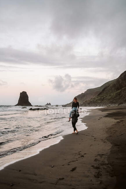 Homme méconnaissable portant une femme sur les épaules près de la mer — Photo de stock