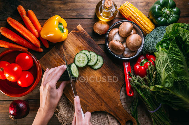 Human hands cutting fresh vegetables on wooden chopping board on kitchen table — Stock Photo