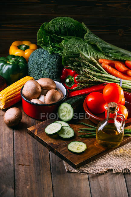 Surtido de verduras frescas crudas y utensilios en la mesa de cocina de madera - foto de stock