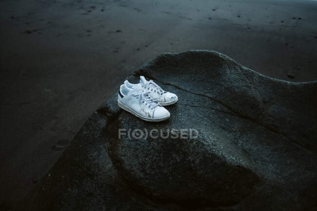 Weiße Turnschuhe auf grobem grauen Stein am nassen dunklen Strand — Stockfoto
