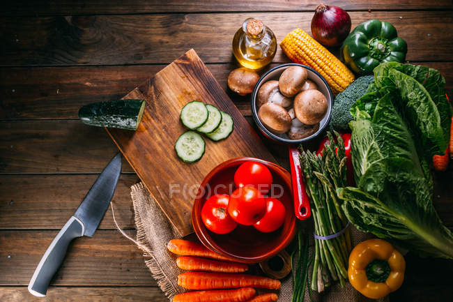 Surtido de verduras frescas crudas y utensilios en la mesa de cocina de madera - foto de stock