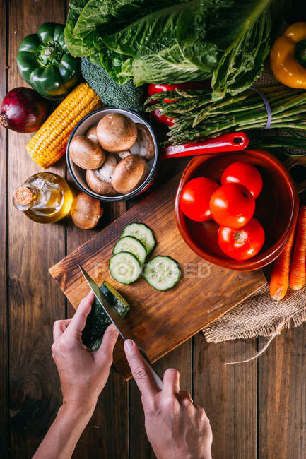 Mains humaines coupant des légumes frais sur planche à découper en bois sur table de cuisine — Photo de stock