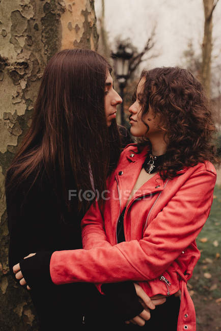 Uomo dai capelli lunghi che abbraccia e bacia donna vicino all'albero — Foto stock
