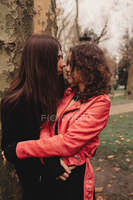 Довгошерстий чоловік обіймає і цілує жінку біля дерева — стокове фото