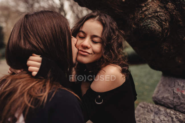 Длинноволосый мужчина обнимает и целует женщину возле дерева — стоковое фото