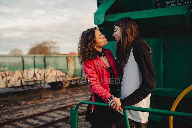 Hombre de pelo largo abrazando y besando a mujer cerca del tren - foto de stock