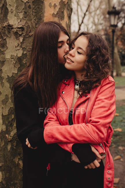 Homem de cabelos compridos abraçando e beijando mulher perto da árvore — Fotografia de Stock