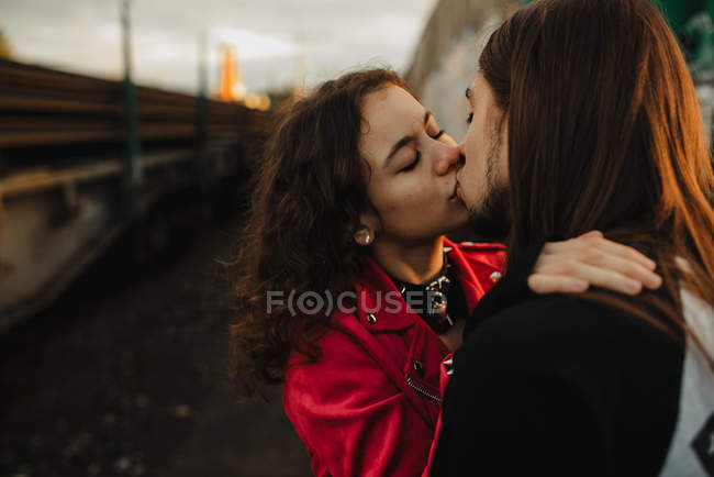 Длинноволосый мужчина обнимает и целует женщину возле поезда — стоковое фото